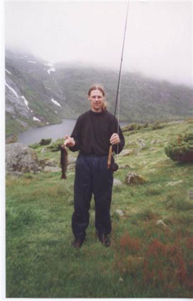 Fisker som holder fluestang i venstre hånd og en ørret i den høyre