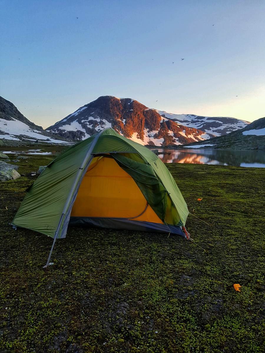 Telt foran et vann og et lite fjell hvor kveldsolen blir reflektert.