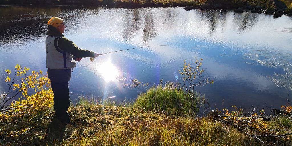 Fluefisker som kaster i vann hvor solen speiler seg.