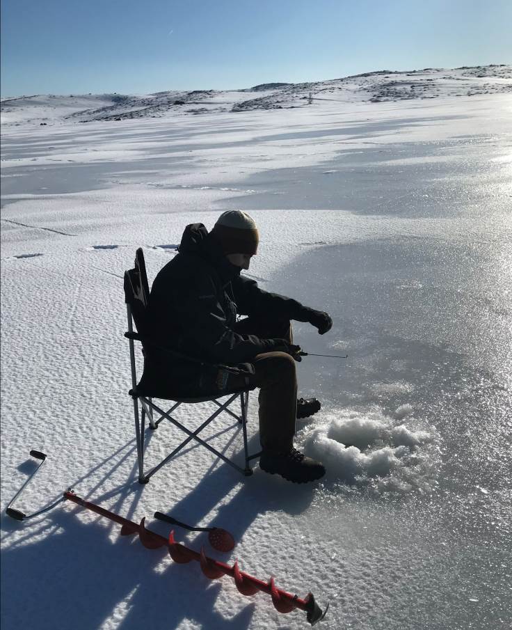 Mann sitter på stol og pilker på isen.