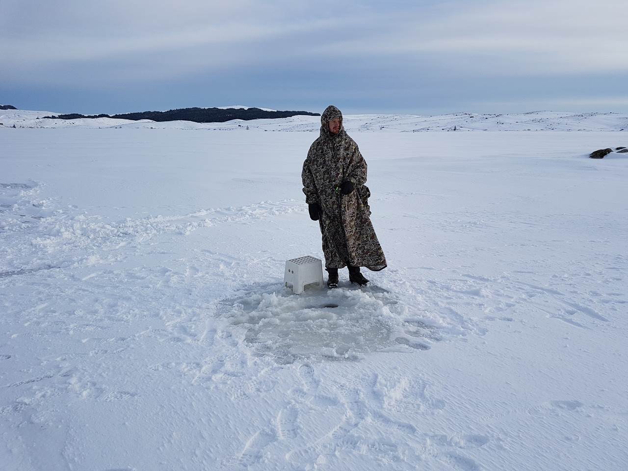Mann som står foran hull i isen med fjellduk på.