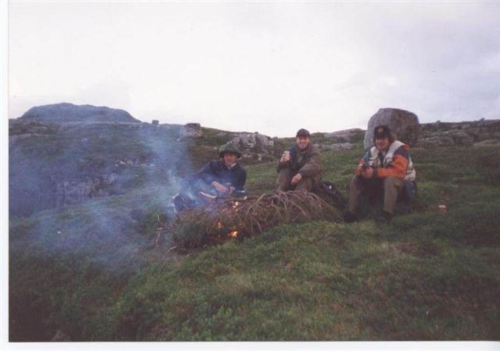 Tre menn som sitter rundt et bål.